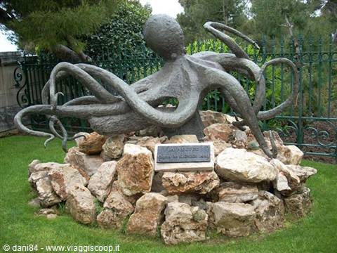 Bronze octopus statue on rocks in a park with green fence
