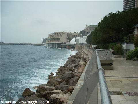 Monaco seafront with rocky shore, metal railing and choppy sea under grey sky