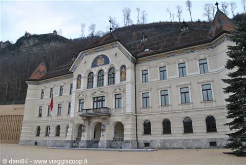 White building with golden decorations and red flag beneath wooded hillside