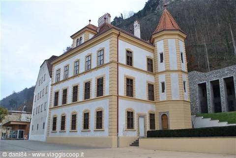 Yellow and white palace with corner turret, forested mountain rising behind