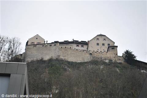 Vaduz Castle atop a wooded hill, stone walls under grey sky