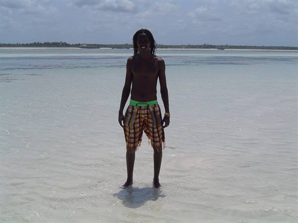 Young shirtless man in yellow kikoi shorts standing in shallow turquoise water