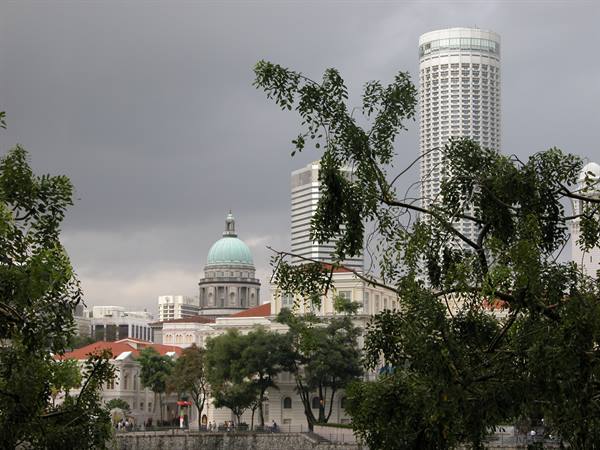 Green dome of the old courthouse among trees, cylindrical skyscraper, cloudy Singapore sky