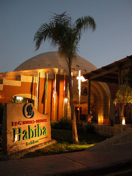 Wooden Habiba hotel sign in front of an illuminated domed building and palm tree