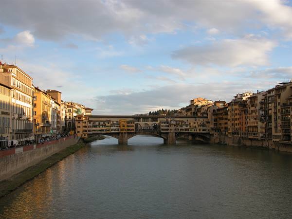 Ponte Vecchio over the Arno in Florence, colorful houses under golden clouds