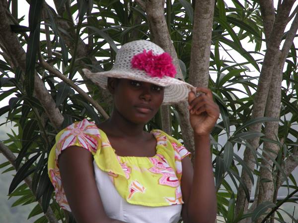 Young woman in straw hat with pink flower among green trees