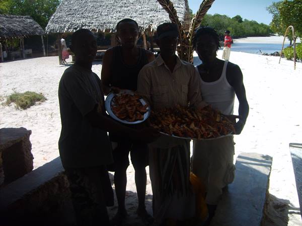 Four men holding trays of fresh caught fish on shaded beach