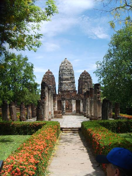 Ancient stone prangs at Sukhothai temple, path lined with flowering bushes
