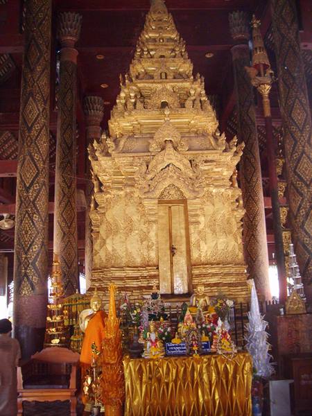 Golden shrine inside Wat Phra That Lampang Luang with offerings and a monk in orange