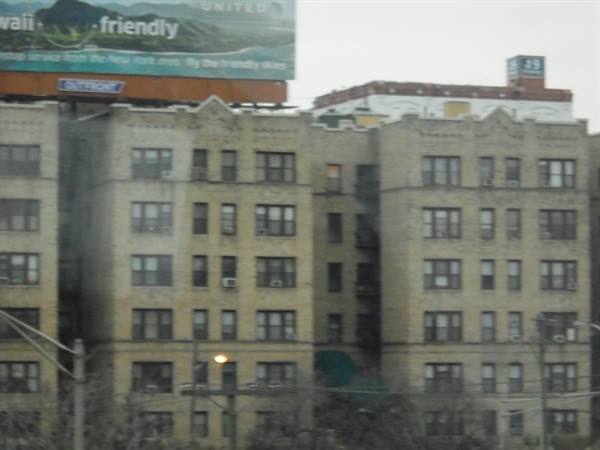Yellow brick apartment building topped by a billboard, overcast sky