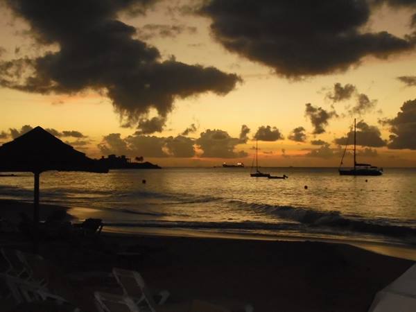Silhouetted umbrella and lounge chairs on beach with anchored boats