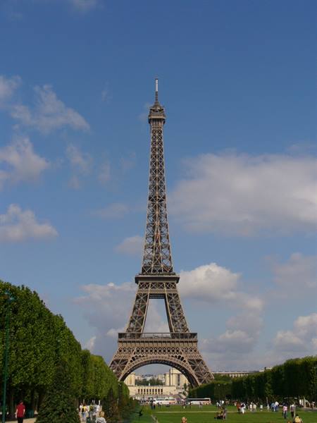 The Eiffel Tower in iron against blue sky, visitors on the grass at Champ de Mars