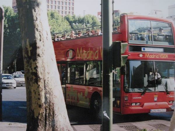 Red double-decker Madrid Vision tour bus with tourists on open top deck