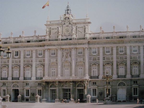 Royal Palace of Madrid, stone facade with Spanish flag and tourists in the square