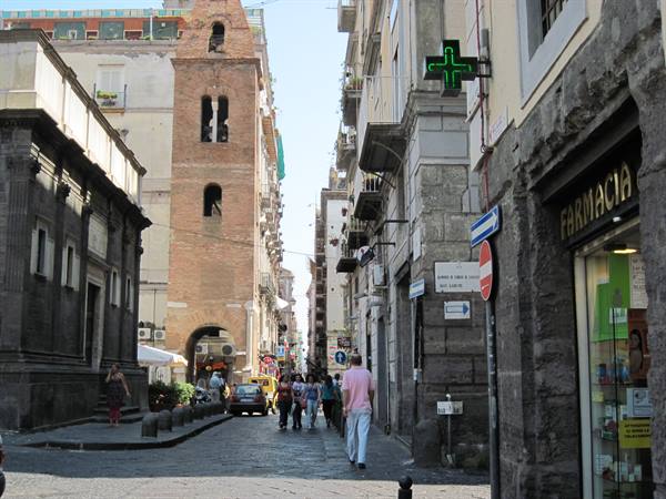 Brick bell tower over street with green pharmacy sign in Naples