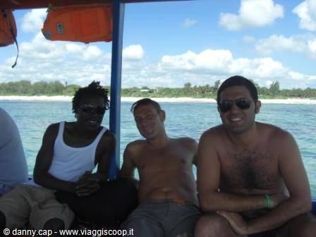 Three smiling men on a boat, turquoise sea and white tropical beach behind