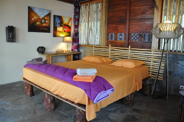 Wooden bed on log legs with orange sheets and purple blanket