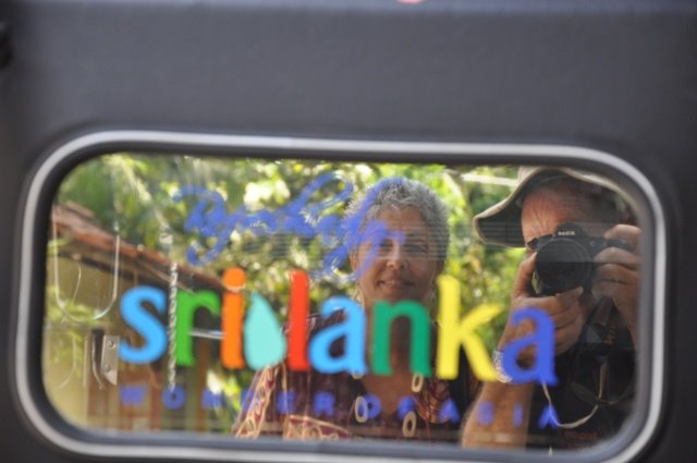 Reflections on the train window: photographer with camera and colorful Sri Lanka sign