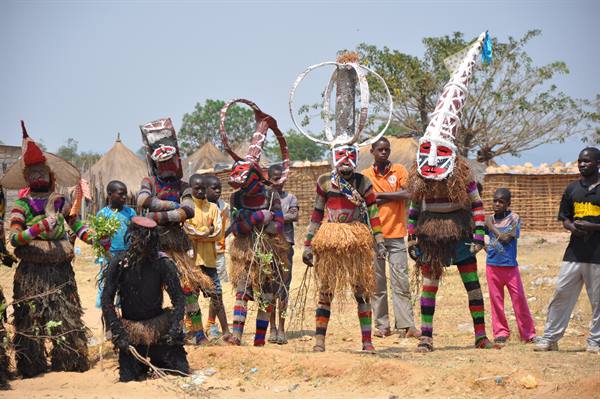 Masked dancers in straw and raffia costumes perform before villagers