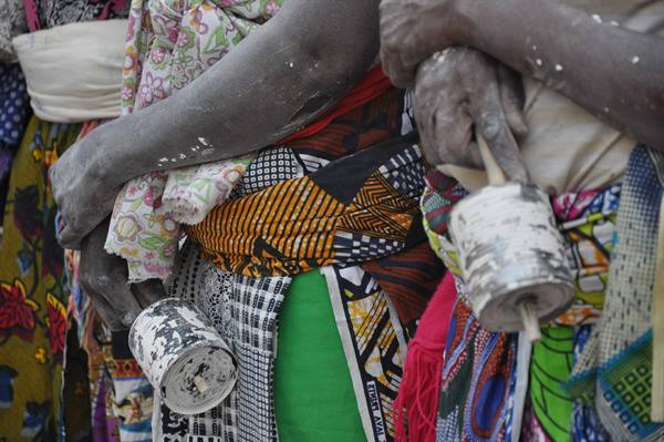 Dark arms with bracelets, colorful fabrics, hands holding paint-splattered tin cylinders