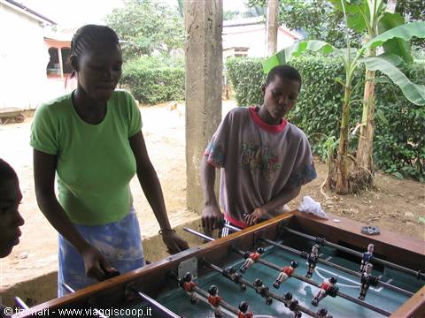 Two young people play foosball under a porch near banana trees