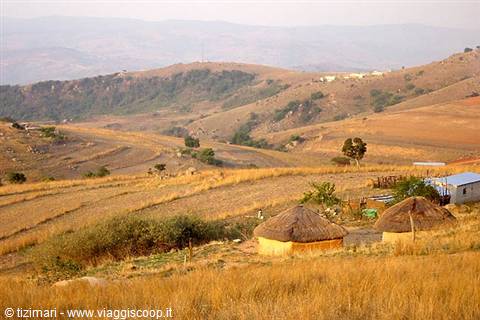 Thatched-roof huts on dry golden hills, two women walking