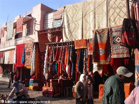 Souk with Berber carpets hanging between stalls, people strolling, bright sunlight