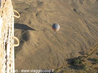 Hot air balloon flying over arid hills, wicker basket edge in foreground