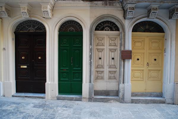 Four wooden doors in brown, green, white and yellow between limestone arches