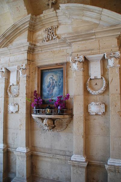 Stone altar with Madonna painting and purple flowers in baroque church