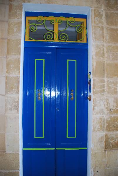 Blue door with green trim and yellow wrought iron fanlight, stone wall