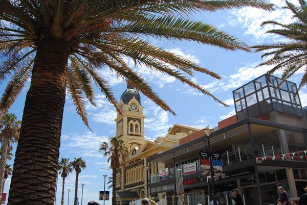 Torre civica con orologio tra le palme, cielo azzurro, persone passeggiano, Glenelg