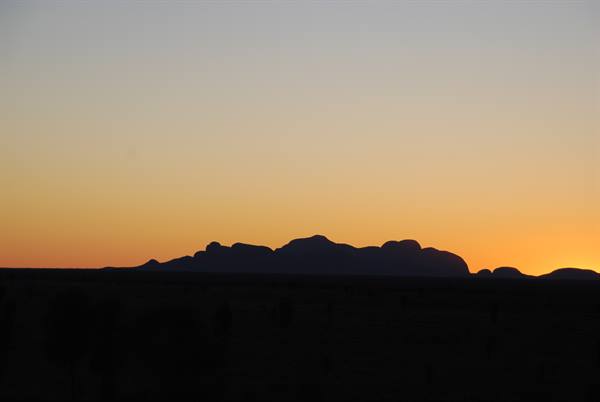 Le sagome scure delle Kata Tjuta emergono nel cielo arancio dell'outback