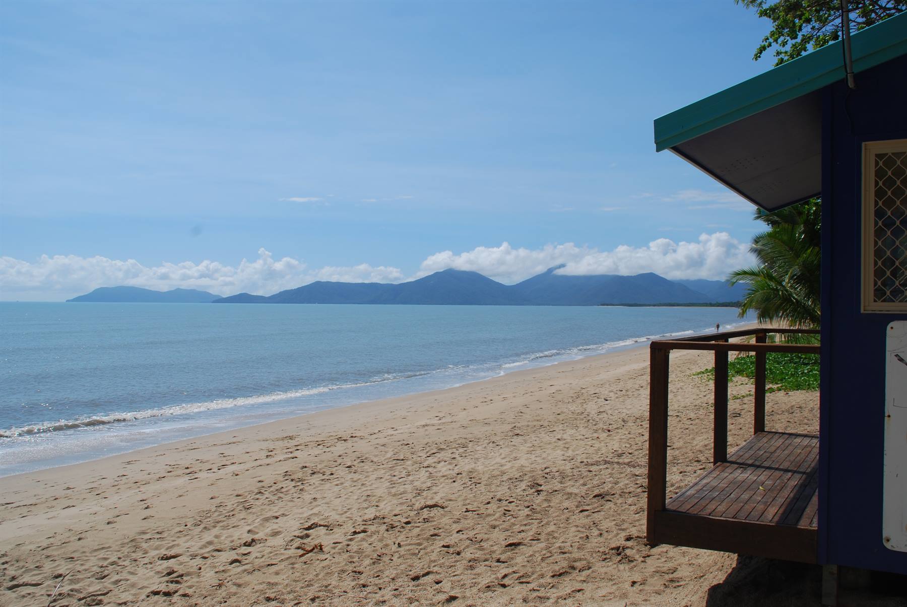 Spiaggia sabbiosa con chiosco di legno, mare turchese e monti lontani, Cairns