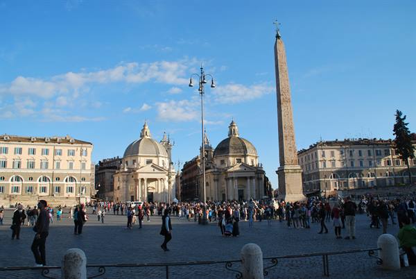 Tourists stroll through Piazza del Popolo past the Egyptian obelisk and twin churches