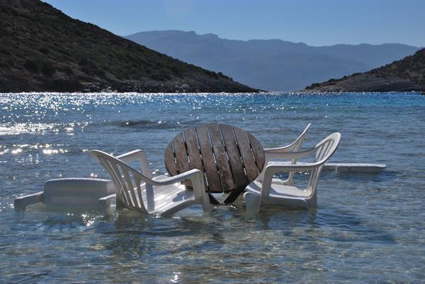 Wooden table and white plastic chairs half-submerged in clear water between hills