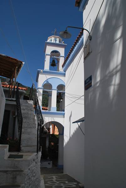 white and blue belfry among narrow alleys, stone stairs, clear blue sky