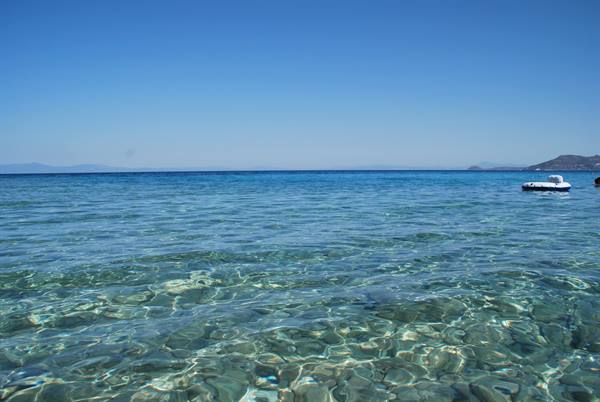 Clear turquoise water over visible pebbles, white pedal boat floats, cloudless sky