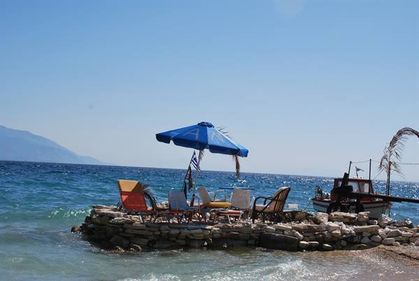 Blue umbrella and chairs on stone jetty, Greek boat moored, turquoise sea