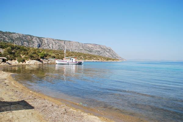 White fishing boat moored in clear turquoise bay, sandy beach, rocky hills under blue sky