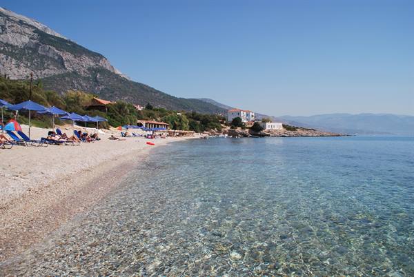 Pebble beach with blue umbrellas, crystal clear water and mountains behind