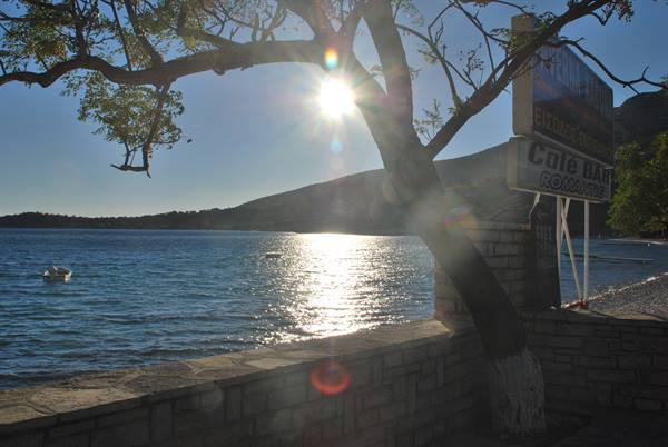 Low sun on the sea behind a tree, stone wall and Caffe Bar sign