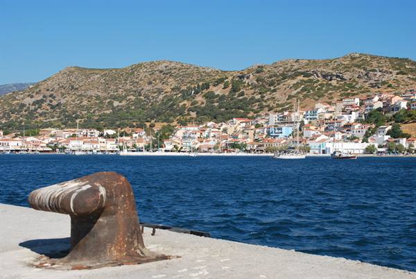 Rusty mooring bollard on pier, harbor town with boats behind