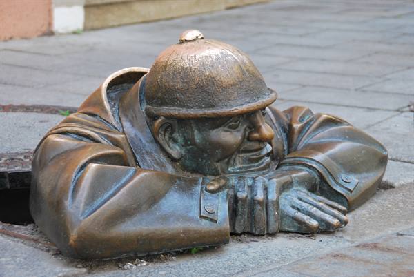 Bronze statue of a man in a helmet peeking from a manhole