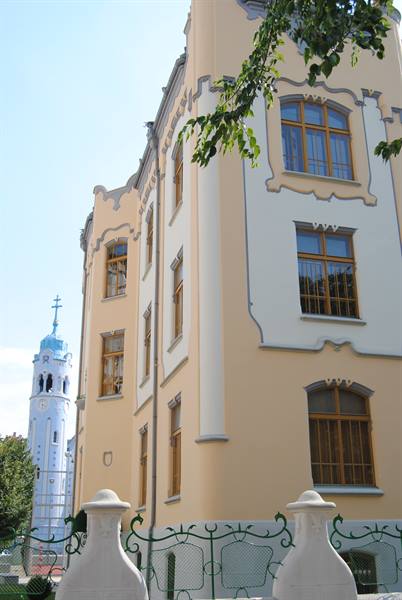 Yellow Art Nouveau building with wooden windows, behind the Blue Church's pale blue tower