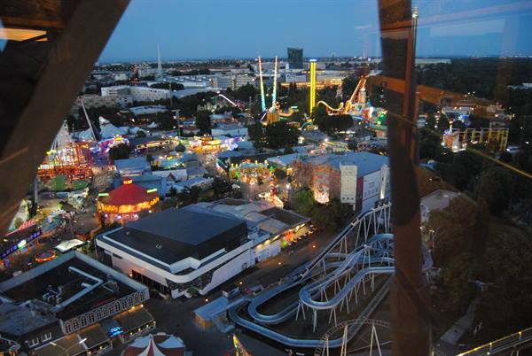 Night amusement park seen from above: lit rides, roller coaster and pavilions
