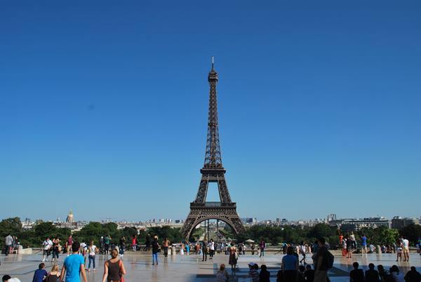 The wrought-iron Eiffel Tower under blue sky, tourists on the square