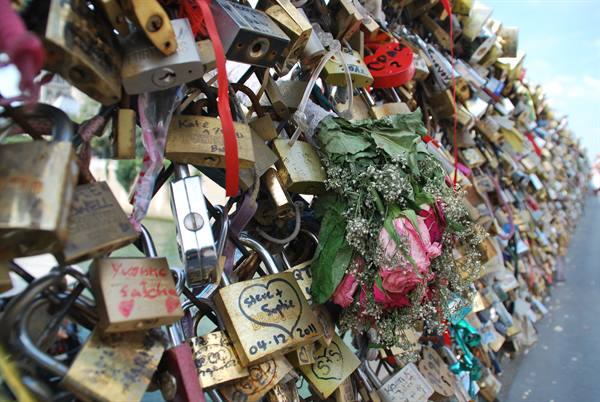 Brass love locks with inscribed hearts cover the railing, bouquet of roses hanging