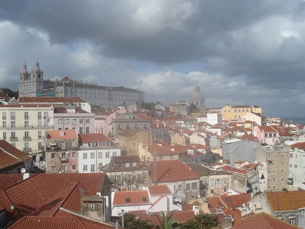 Red rooftops of Alfama under grey clouds, with churches and colorful houses in Lisbon
