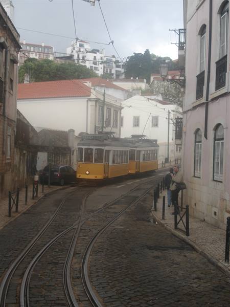 Yellow tram on cobblestone tracks among white houses in Lisbon
